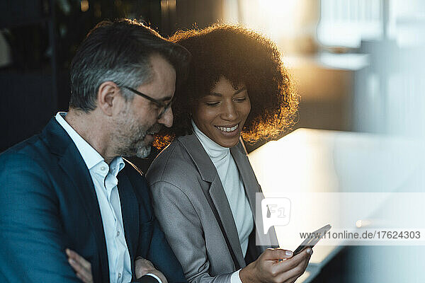 Smiling businesswoman sharing smart phone with colleague in office