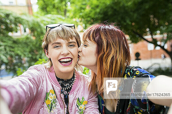 Young woman kissing cheerful friend