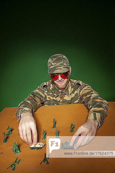 Young military soldier with army figurines and tanks on table