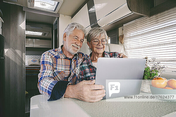 Smiling senior couple using laptop in camper van