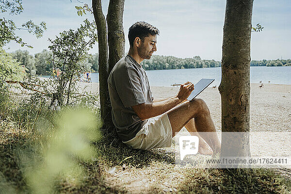 Man using tablet PC at lakeshore on weekend