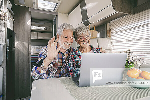 Happy senior couple waving on video call through laptop at motor home