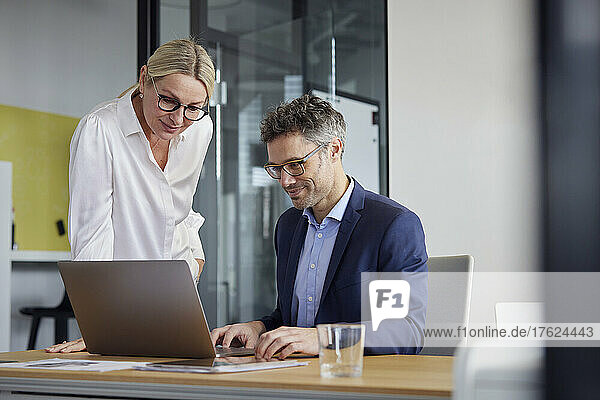 Businesswoman watching colleague working on laptop in office