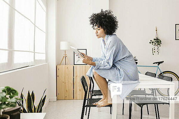 Young woman sitting on table using tablet PC at home