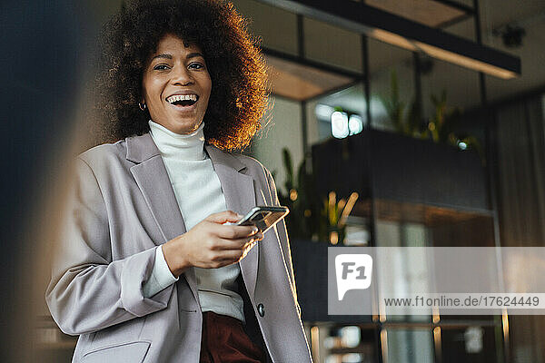 Cheerful businesswoman with mobile phone at work place