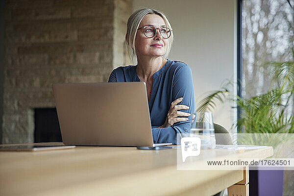 Blonde Frau mit Brille sitzt mit Laptop am Tisch