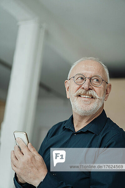 Smiling senior man with mobile phone in office