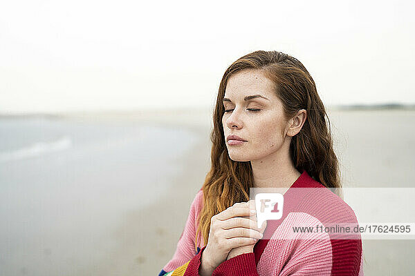 Beautiful young redhead woman standing with eyes closed at beach