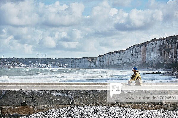 Woman sitting on wall by sea at vacation