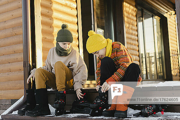 Jungen mit Schlittschuhen sitzen im Winter auf der Veranda eines Hauses