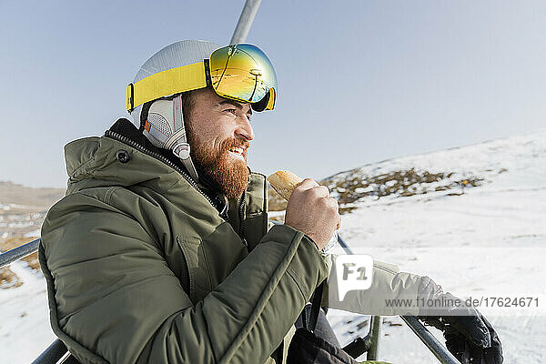 Smiling young man eating snack on ski lift