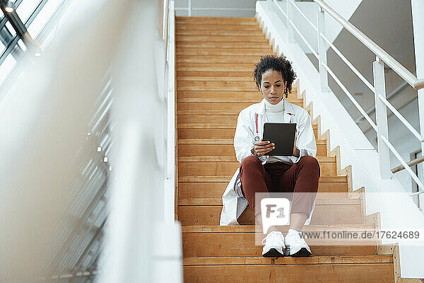 Doctor using tablet computer sitting on steps at hospital