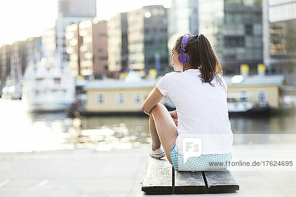 Woman with headphones sitting on bench at waterfront