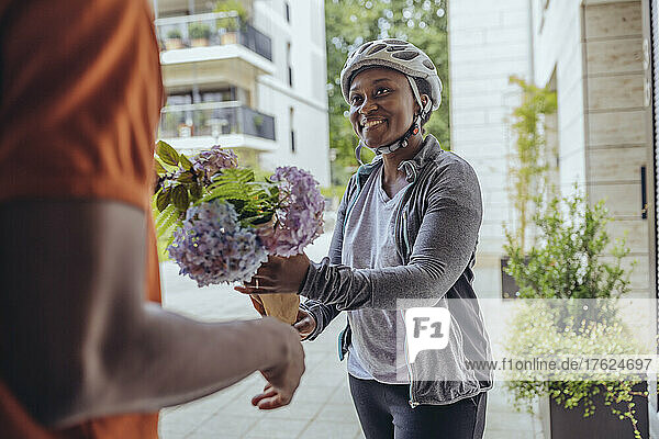 Smiling delivery woman giving flower bouquet to man at doorway