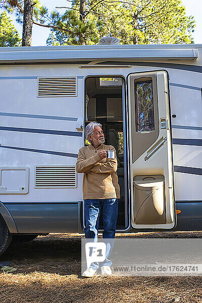 Senior man with coffee cup standing by door of motor home