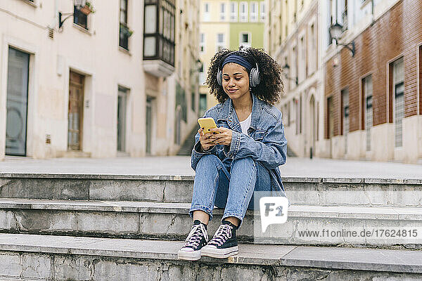 Woman listening music through headphones and using smart phone on steps