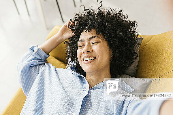 Happy young woman with eyes closed lying on sofa at home