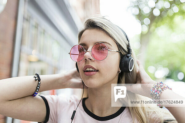 Teenage girl with hand in hair listening music through wireless headphones