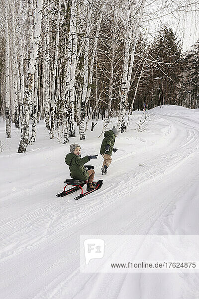 Boys tobogganing on snow in winter forest