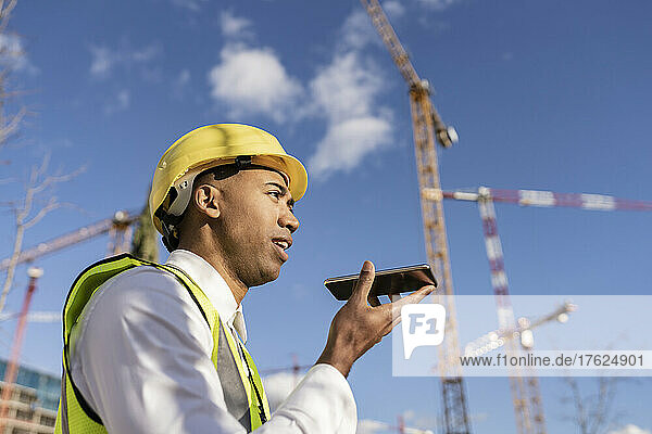 Engineer talking on smart phone through speaker at construction site on sunny day