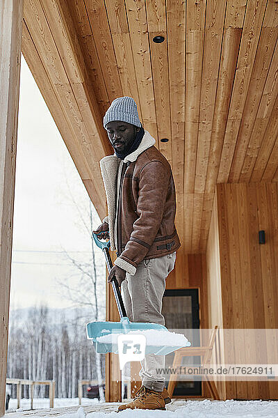 Man holding shovel with snow on porch outside house