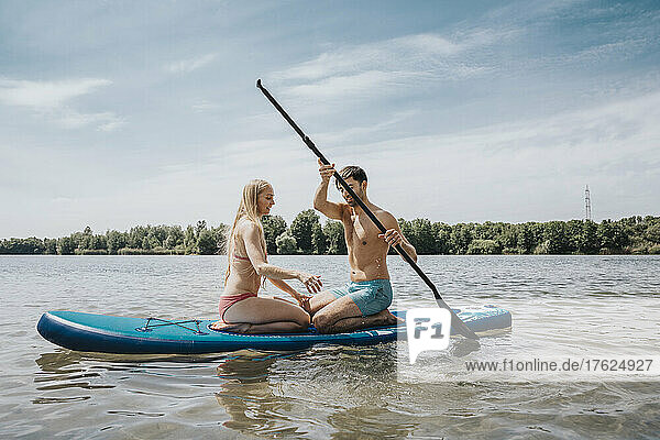 Man paddleboarding with woman on lake at weekend