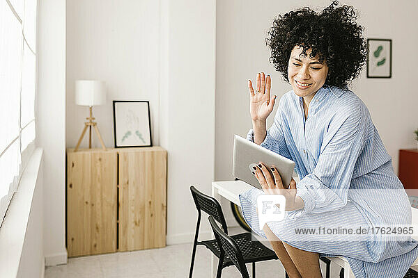 Happy woman waving hand on video call through tablet PC at home