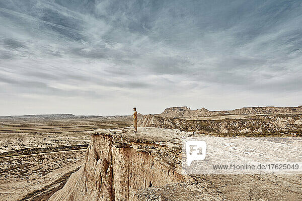 Woman standing on cliff in desert landscape under cloudy sky