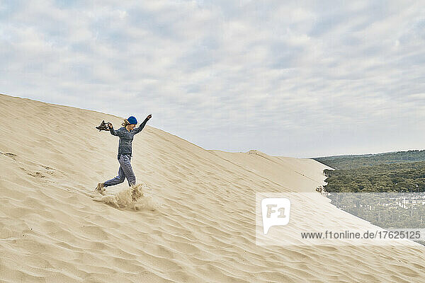 Cheerful woman running on sand dune