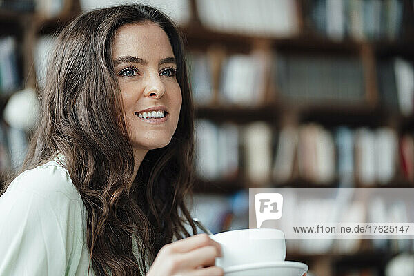 Smiling woman with coffee cup day dreaming in cafe