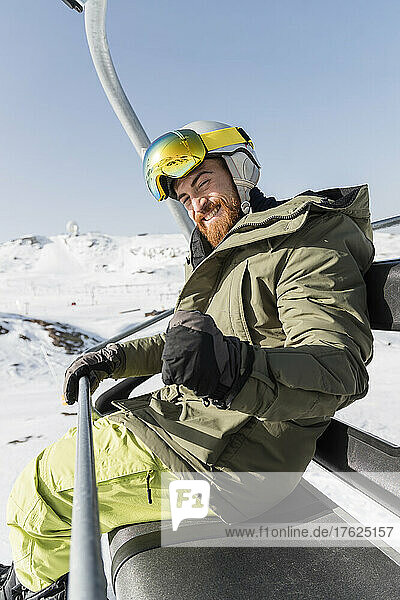 Happy young man gesturing with closed fist sitting on ski lift