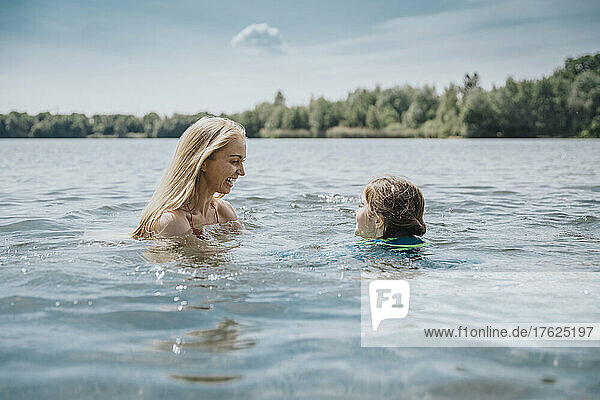 Happy mother and daughter swimming in lake