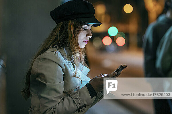 Woman wearing cap using mobile phone at night