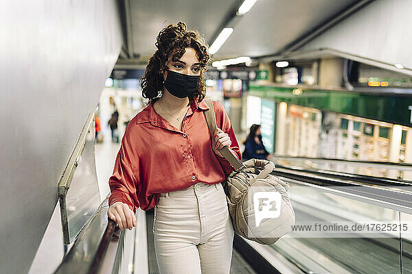 Woman with protective face mask moving up on escalator at station