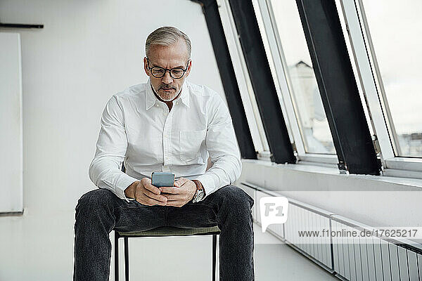 Businessman with eyeglasses text messaging on mobile phone at office