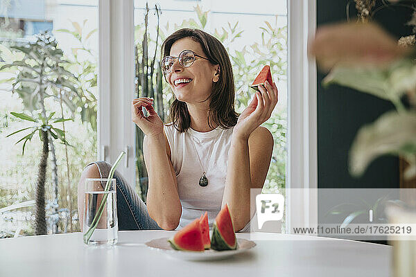 Smiling woman with drinking water and watermelon on table at home