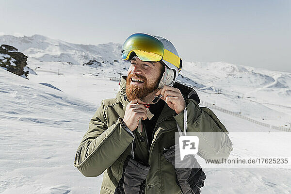Smiling young man with beard fastening skiing helmet