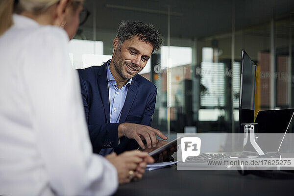 Smiling businessman discussing over tablet PC with businesswoman in office