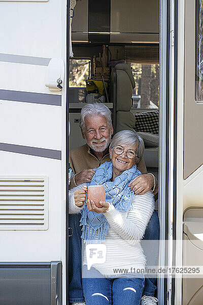 Happy senior couple with coffee cup sitting at door of motor home