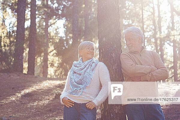 Smiling senior couple leaning on tree trunk in forest