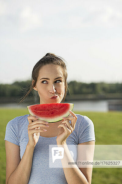 Woman with watermelon slice making face in nature