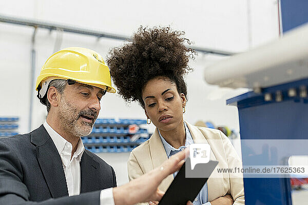Developer showing tablet PC to technician in factory