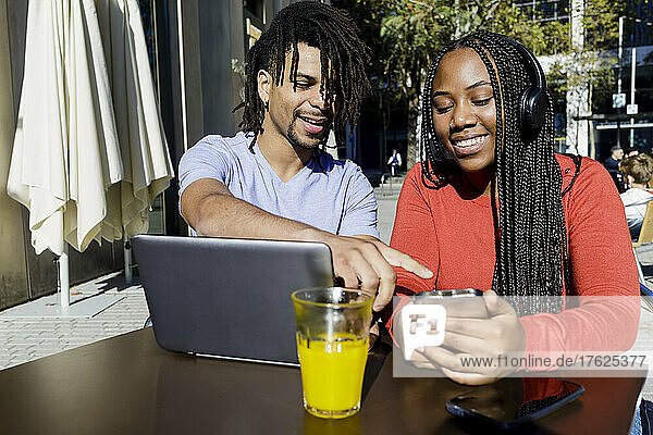 Junger Mann spricht mit Freundin über Smartphone im Straßencafé