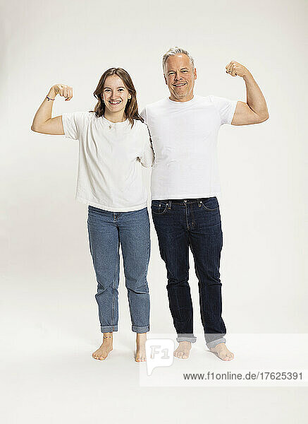 Smiling girl with father flexing muscles against white background