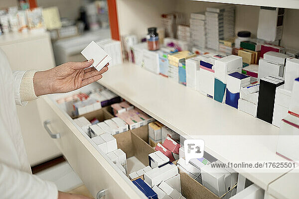 Pharmacist holding box of medicine by drawer at pharmacy store