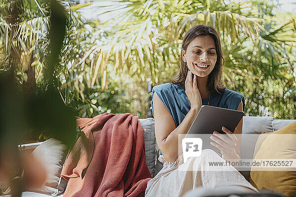 Lächelnder Freiberufler mit Tablet-PC sitzt auf dem Sofa im Garten