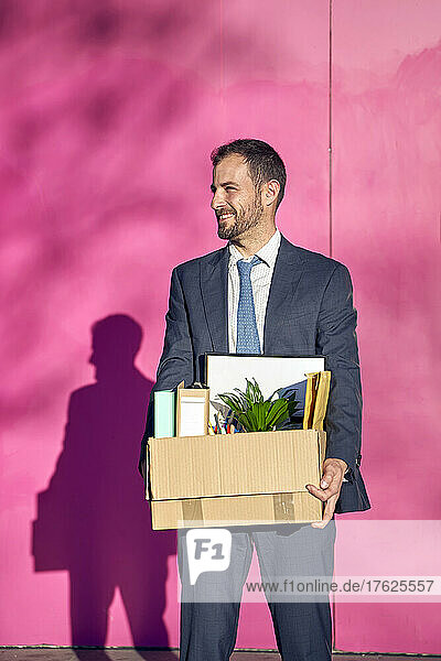 Lächelnder Geschäftsmann mit Kiste vor der Wand