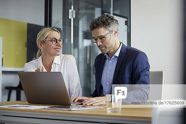 Smiling businesswoman looking at colleague working on laptop in office