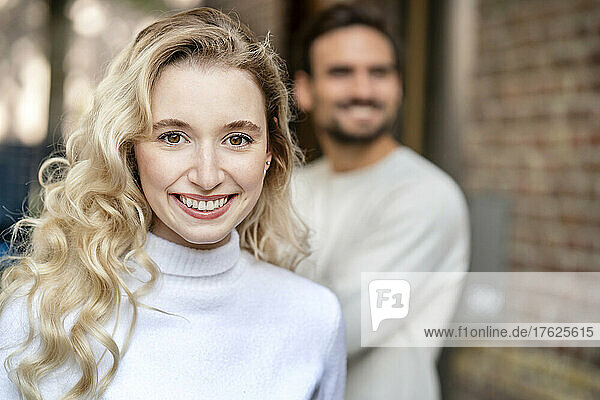 Happy young woman with blond curly hair standing in front of boyfriend