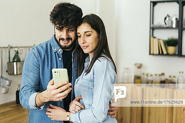 Young couple taking selfie through mobile phone in kitchen at home